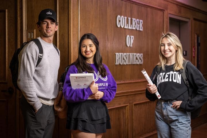Students smiling in front of the College of Business sign