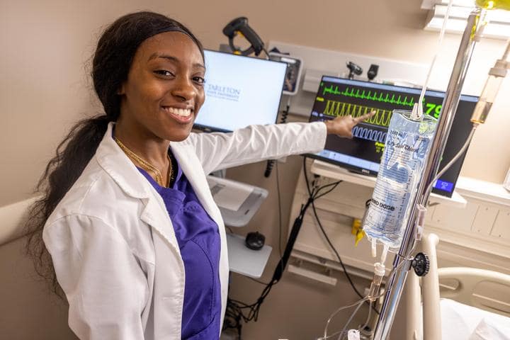 Black Female Student smiling and pointing at a hospital monitor