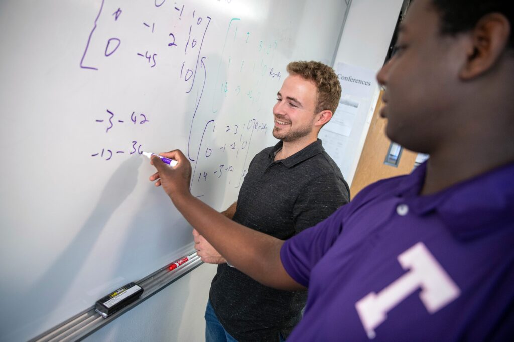 Two male students solving a math problem on a whiteboard