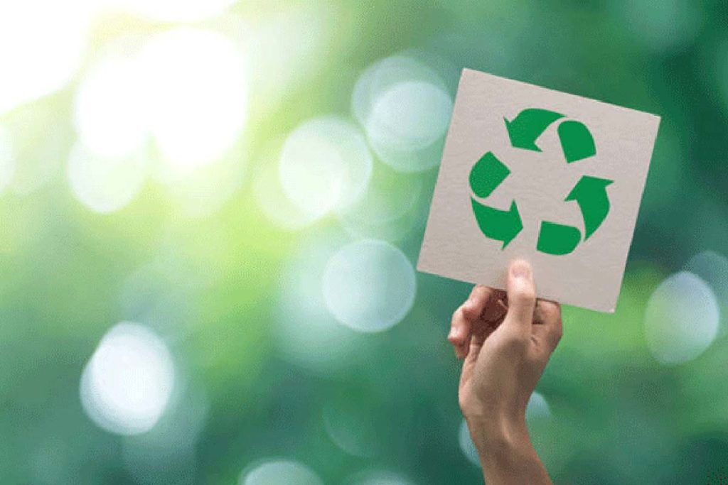 A hand holding up a paper with a recycle symbol on it.