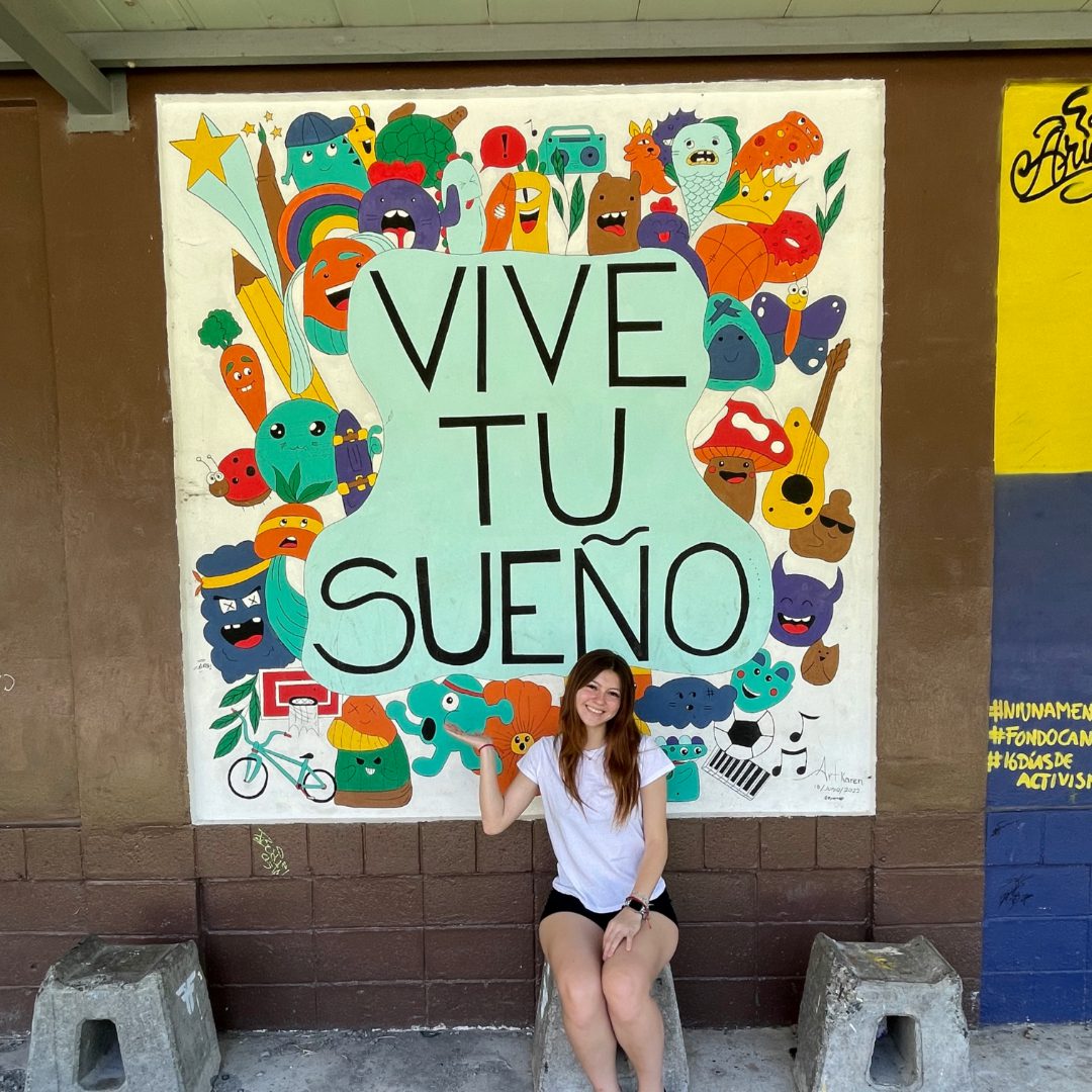 Student in front of a sign in Costa Rica that translates to "Live your dream"