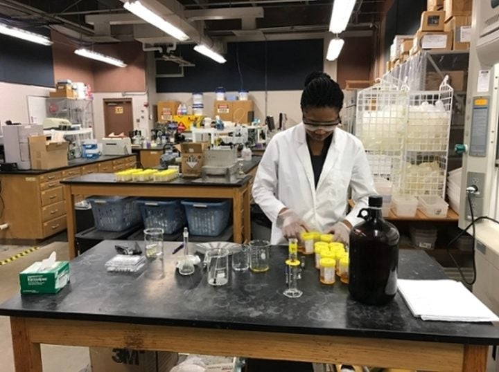 Person in a lab coat working at a laboratory bench with various equipment.