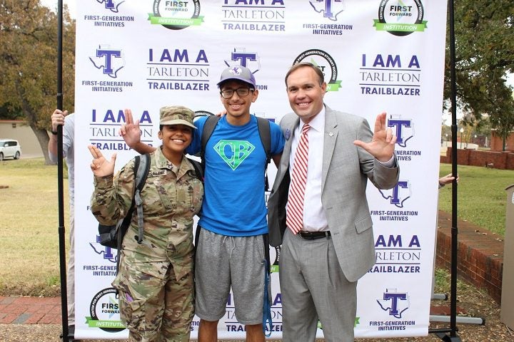 ROTC student, normal civilian student, and the president of the university Dr. Hurley pose in front of a I am a Tarleton Trail Blazer first generation background